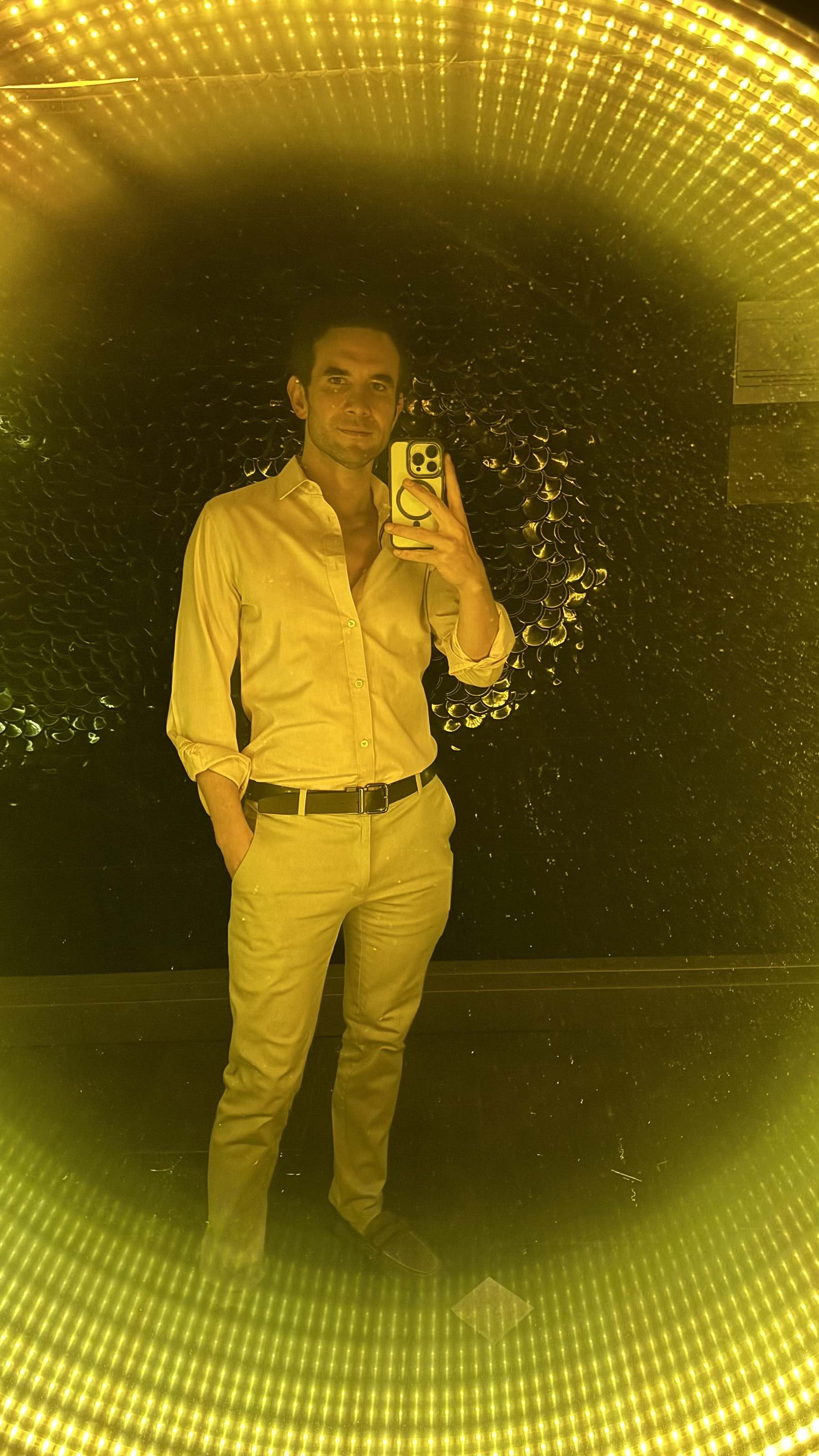 Marco Valdés con traje amarillo grabándose con el celular frente a un espejo con luces doradas