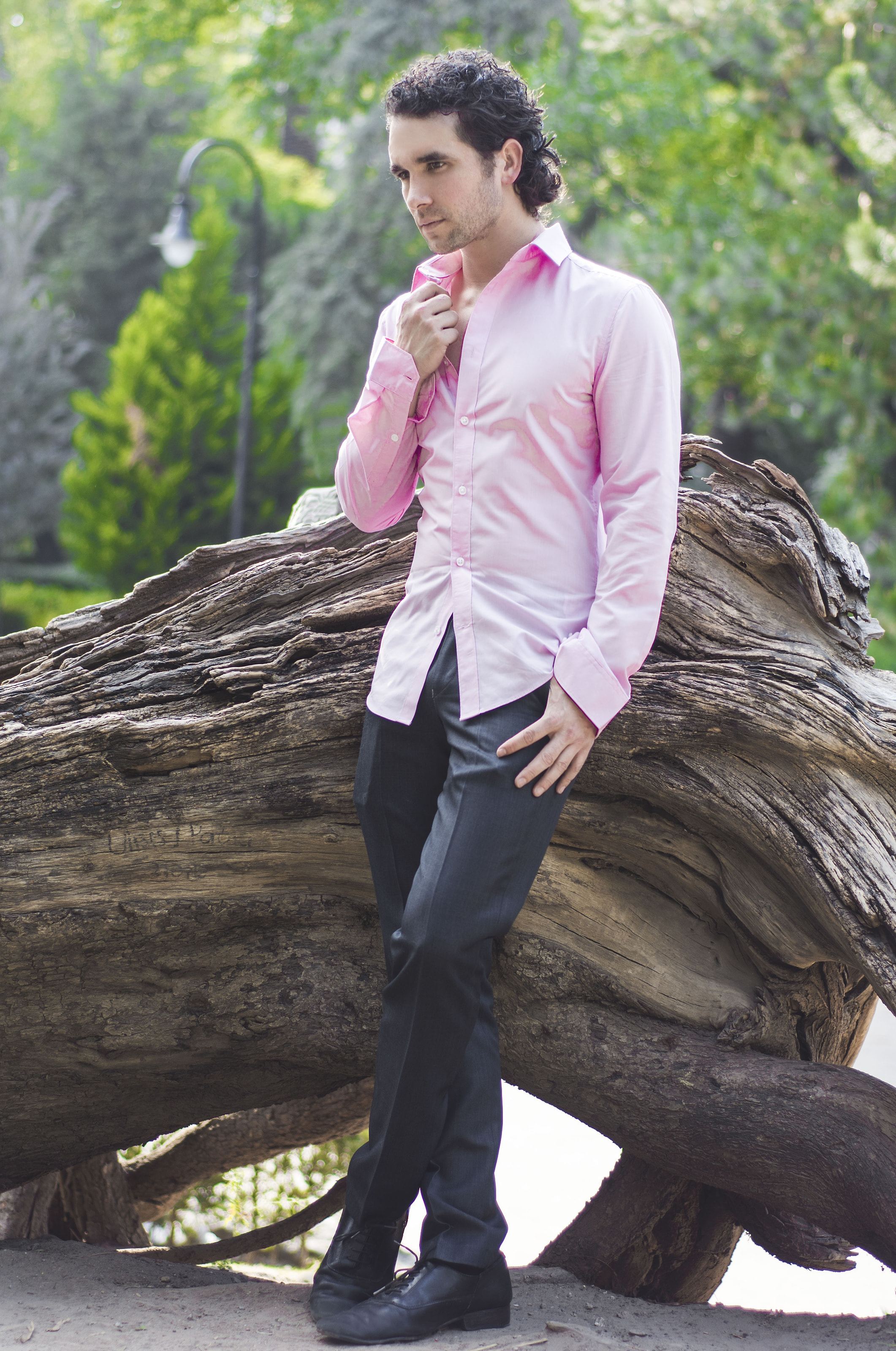 Marco Valdés con camisa rosa, de pie junto a un tronco